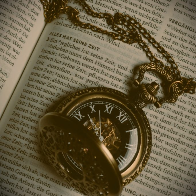 Antik-wirkende, mechanische Taschenuhr mit römischen Ziffern auf einer offenen Bibelseite mit der Überschrift: "Alles hat seine Zeit".