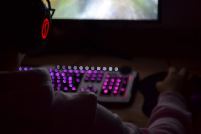 Person am Computer mit Kopfhörern und einer beleuchteten Tastatur. Also ich am Zocken.