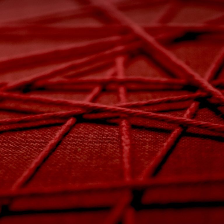 Rote Fäden sind kreuz und quer auf eine rote Fläche angeordnet.