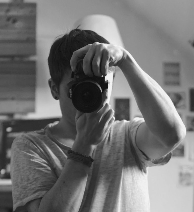 Junger Mann mit Kamera, der sich selbst im Spiegel fotografiert.